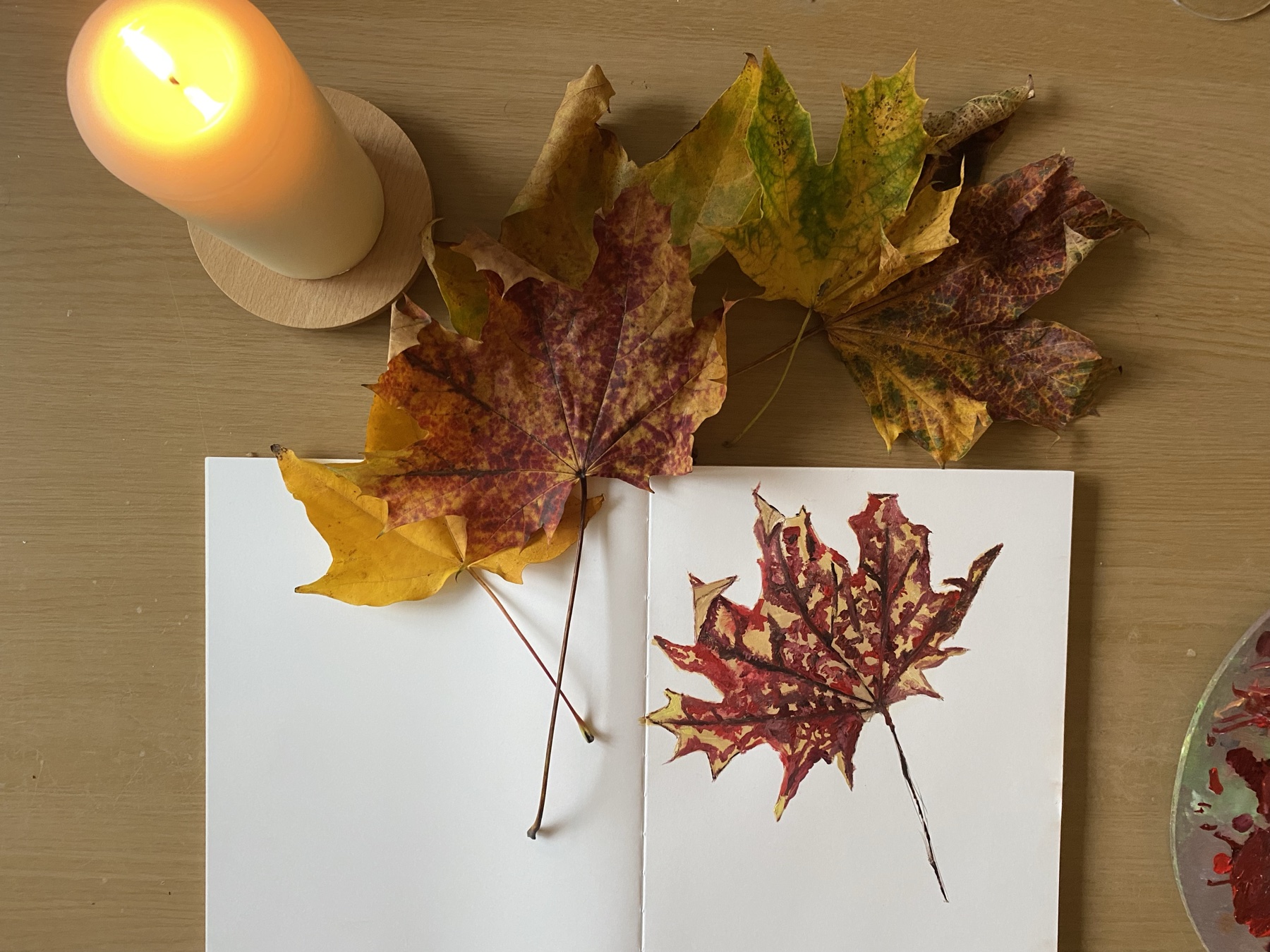 Still life by Jasmin Southgate: autumn maple leaves on a sketchbook, beside a candle
